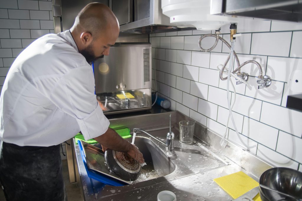 A chef cleans kitchen utensils in a stainless steel sink, maintaining hygiene standards.